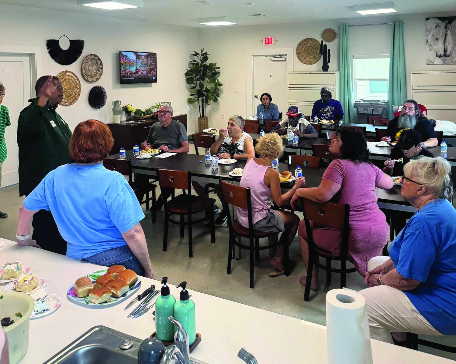 A group of people sit at tables and watch a man speaking.